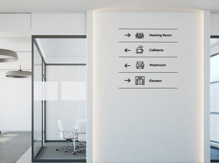 Black wall-mounted directional sign with arrows and icons for meeting room, cafeteria, washroom and elevator